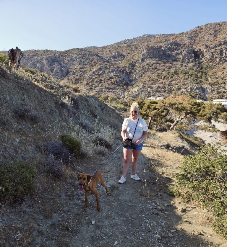 Vrouw met een hond wandelt op een pad in een bergachtig landschap.
