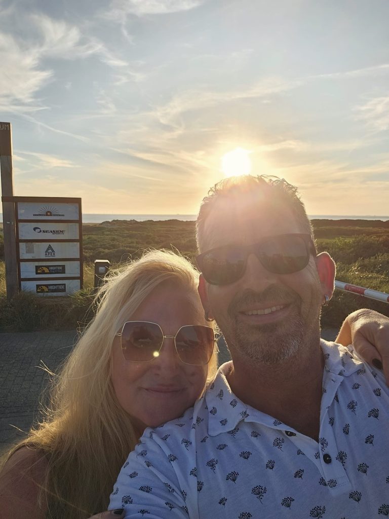Twee mensen poseren samen bij zonsondergang aan het water.