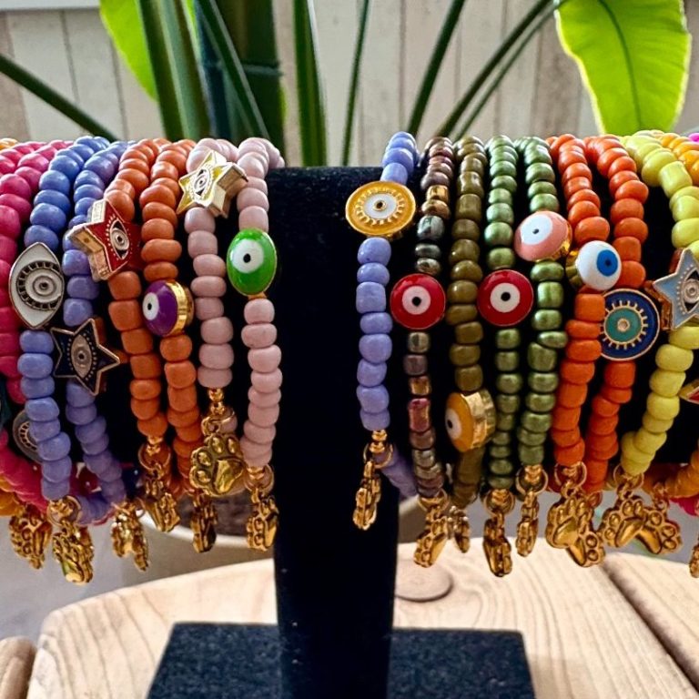 Kleurige armbanden van kralen met diverse details, hangen aan een standaard.